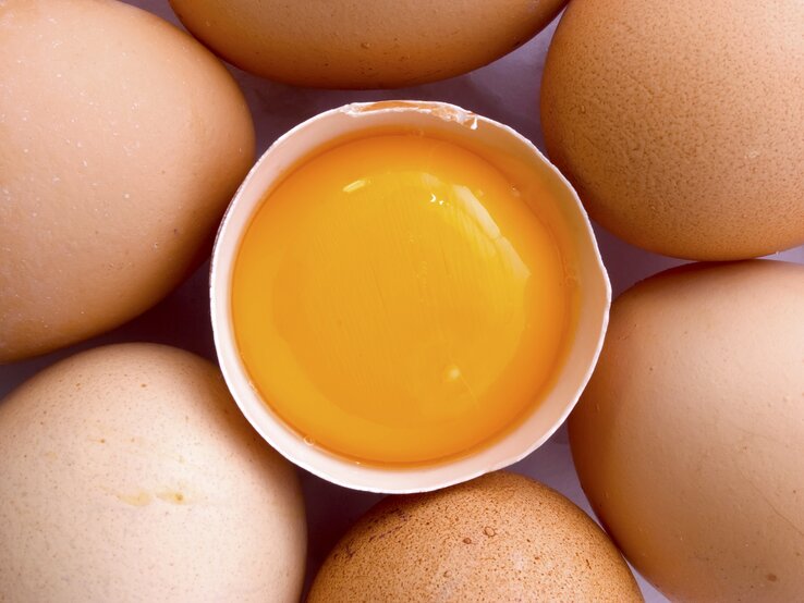 Mehrere Eier liegen um ein aufgeschlagenes Ei. Man sieht das orange Eigelb.